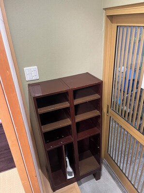 Una habitación de esquina con una estantería de madera, una puerta con reja de metal y un interruptor de luz en la pared.
