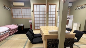 A room with tatami flooring, a wooden table with chairs, a bed with pink bedding, and a shoji screen door.