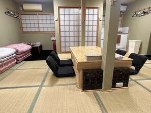 Una habitación con suelo de tatami, una mesa de madera con sillas, una cama con ropa de cama rosa y un puertas correderas shoji.