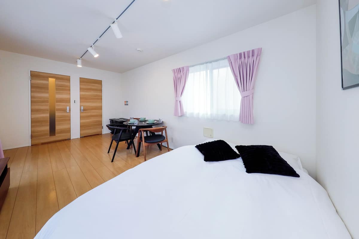 Quarto com uma cama grande, uma escrivaninha com cadeiras e uma janela com cortinas.