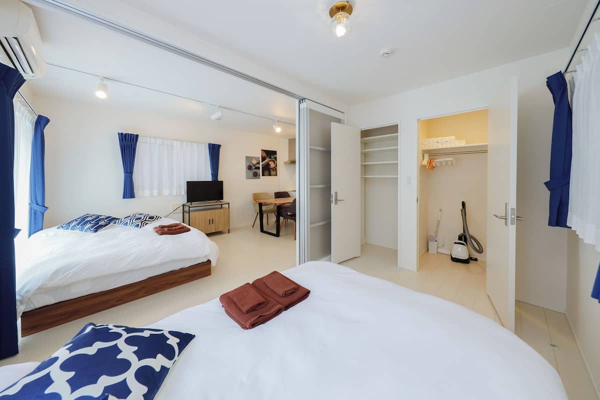 Quarto de hotel com duas camas, uma escrivaninha, uma cadeira, uma televisão, um armário e um aspirador de pó.