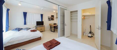 A hotel room with two beds, a desk, a chair, a TV, a closet, and a vacuum cleaner.