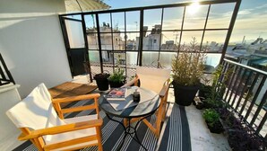 Uma varanda com mesa e cadeiras, plantas em vasos e vista para a cidade.