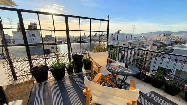 Terraço no telhado com mesa e cadeiras, plantas em vasos e vista para a paisagem urbana.