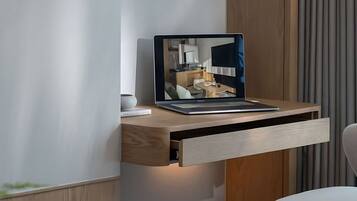 A modern kitchen with a laptop on a wooden shelf, a dining table with a glass of tea, and a chair.