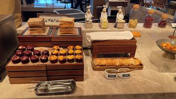 A buffet setup with various food items, including bread, muffins, and jars of nuts and dried fruits.