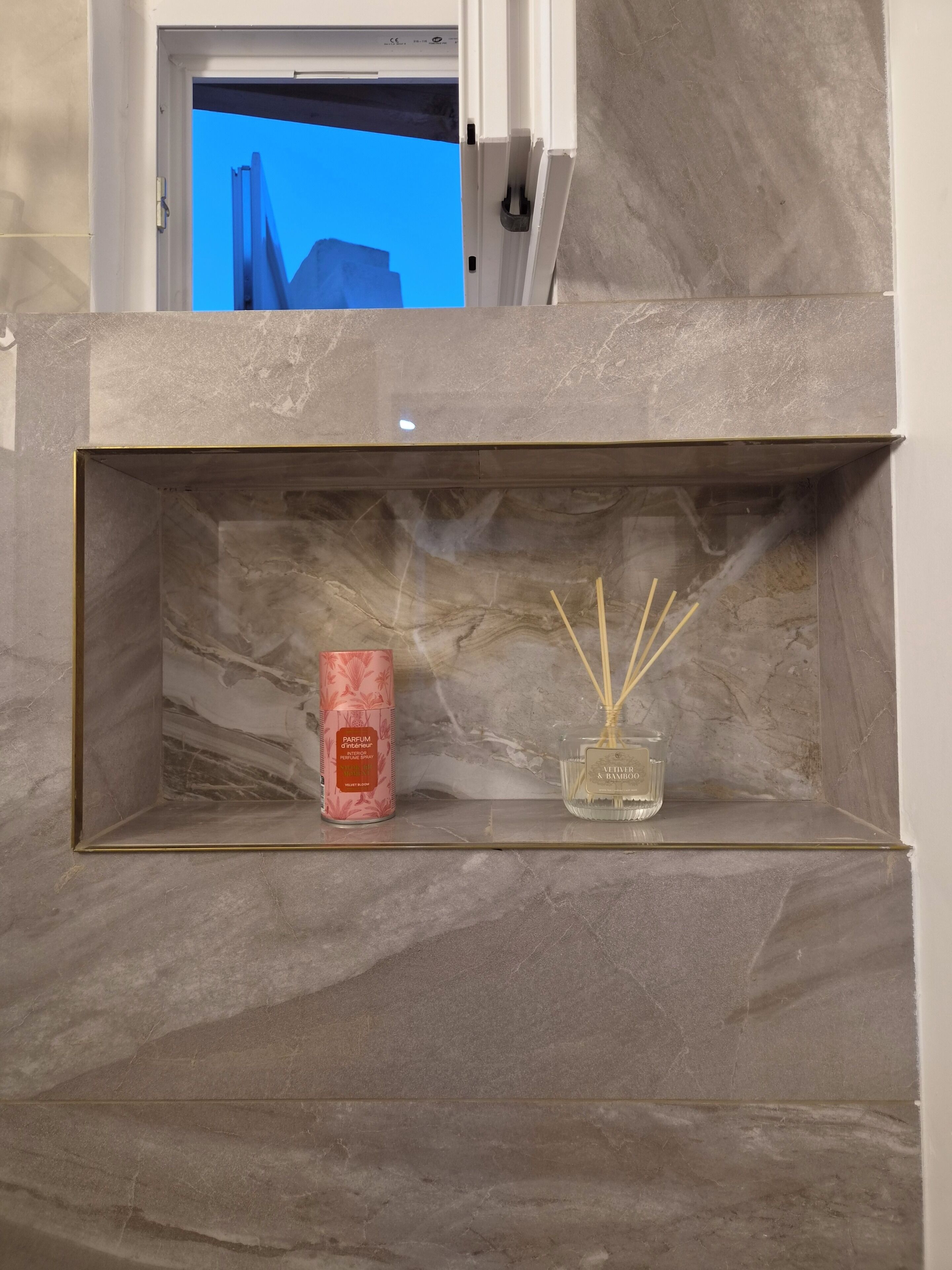 Une étagère à bordure de marbre, ornée d’une bougie parfumée rose et d’un diffuseur à bâtonnets en bambou.