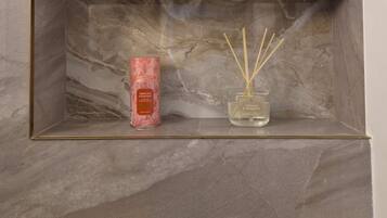 Une étagère à bordure de marbre, ornée d’une bougie parfumée rose et d’un diffuseur à bâtonnets en bambou.