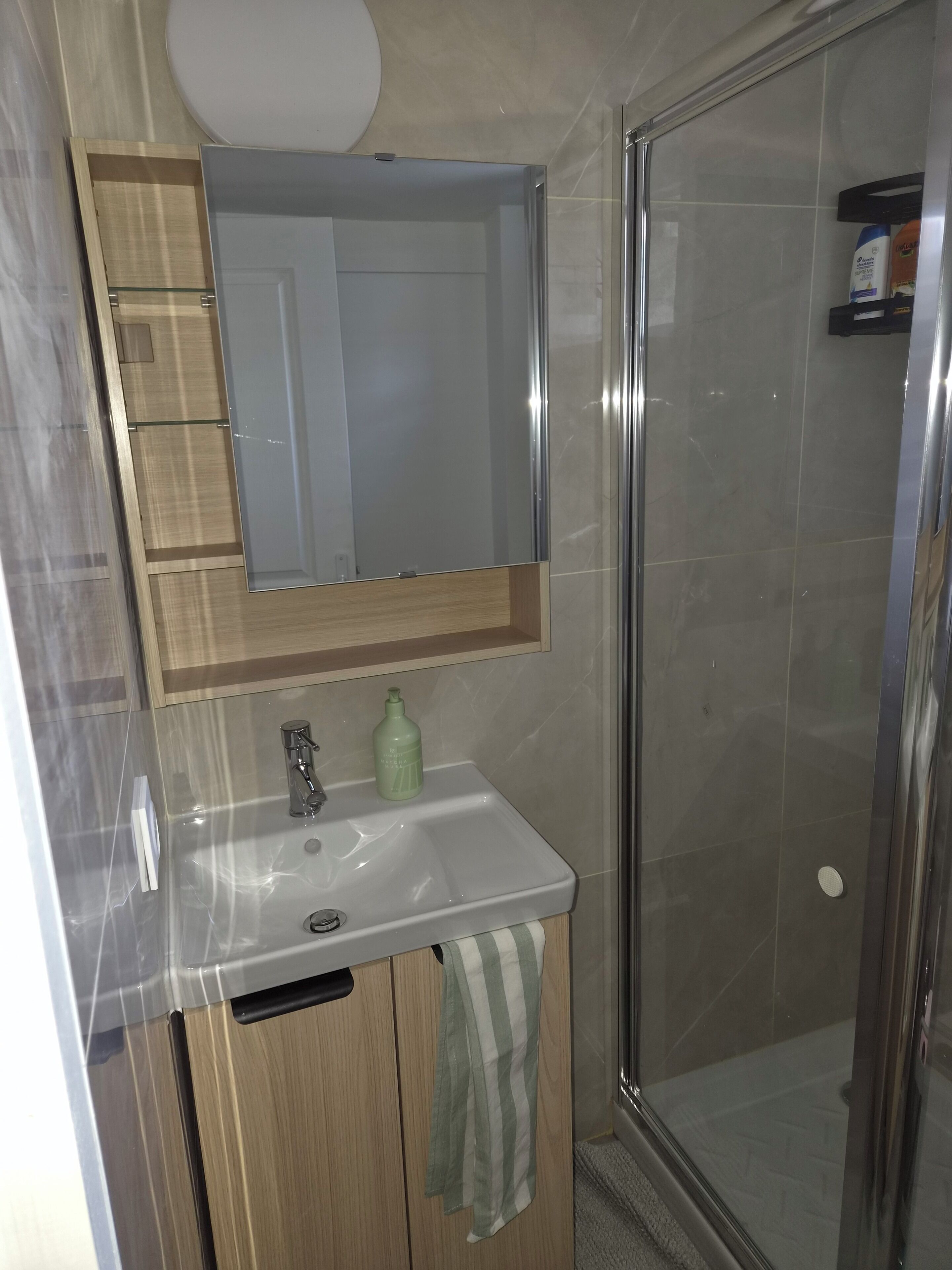 A bathroom with a glass shower enclosure, a sink with a mirror above it, and a towel hanging on the door.