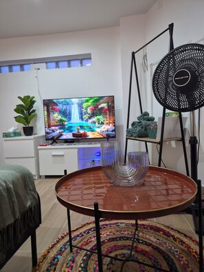 A modern living room with a flat-screen TV, a dining table with a glass centerpiece, a colorful woven rug, and a black fan. - La dolce vita (Champs-sur-Marne)