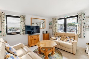 A living room with a sofa, a glass-top coffee table, a TV, and a view of a marina. - 2 Red Brick Building - central Padstow with beautiful estuary  & harbour views (Padstow)