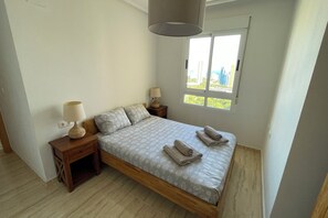 A bedroom with a bed, two bedside tables with lamps, a window with a view, and a wooden floor.