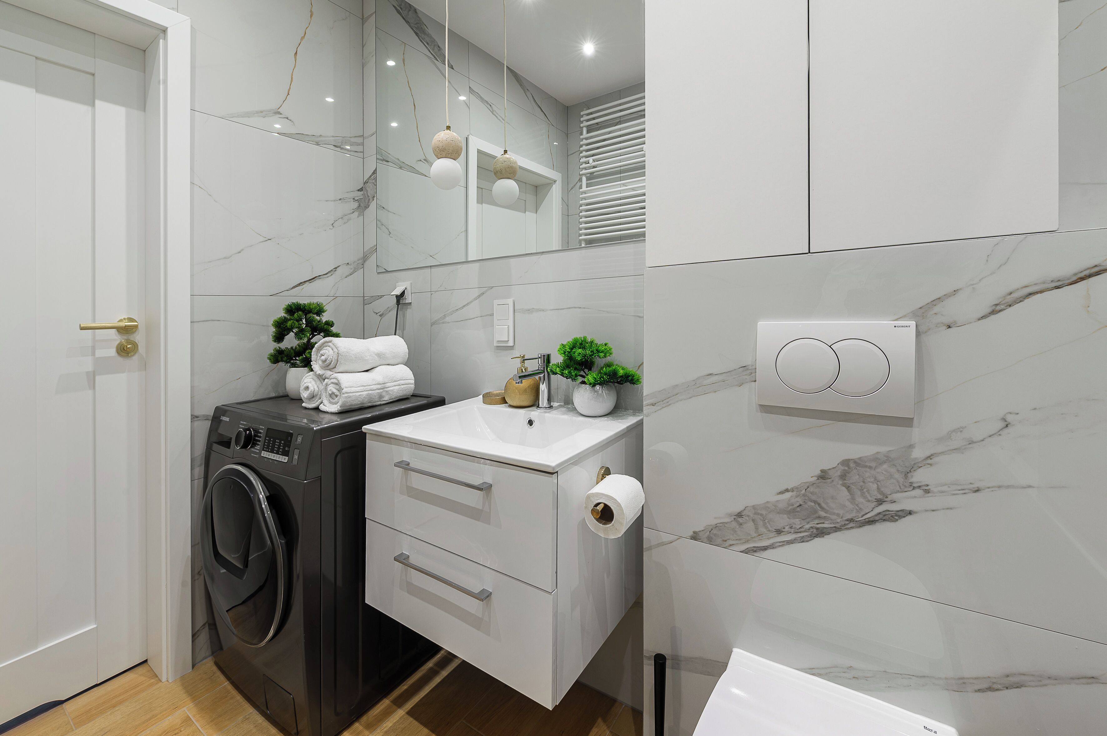 Een moderne badkamer met een wasmachine, een wastafel met spiegel en een toiletrolhouder.