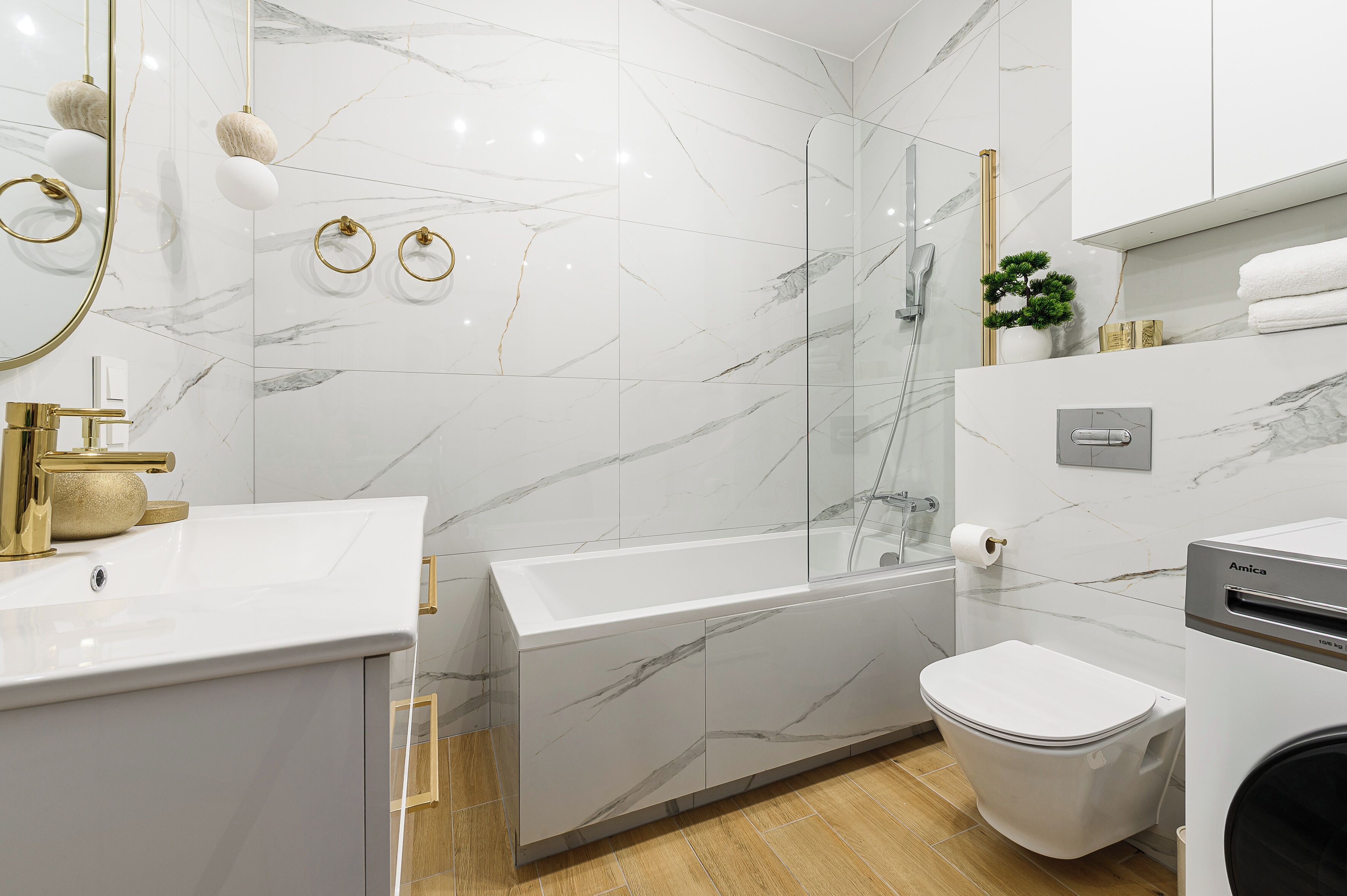 Un baño moderno con un lavamanos blanco, detalles dorados, cabina de ducha de vidrio y un inodoro.