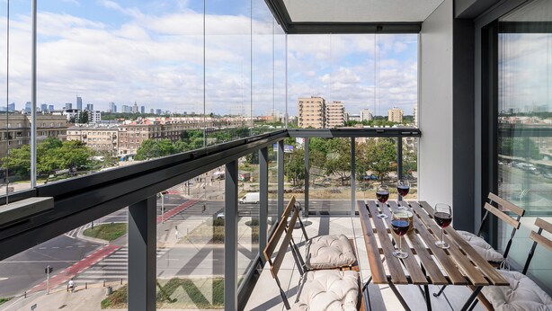 Un balcon donnant sur le paysage urbain, une table avec des verres de vin et un banc agrémenté de coussins.