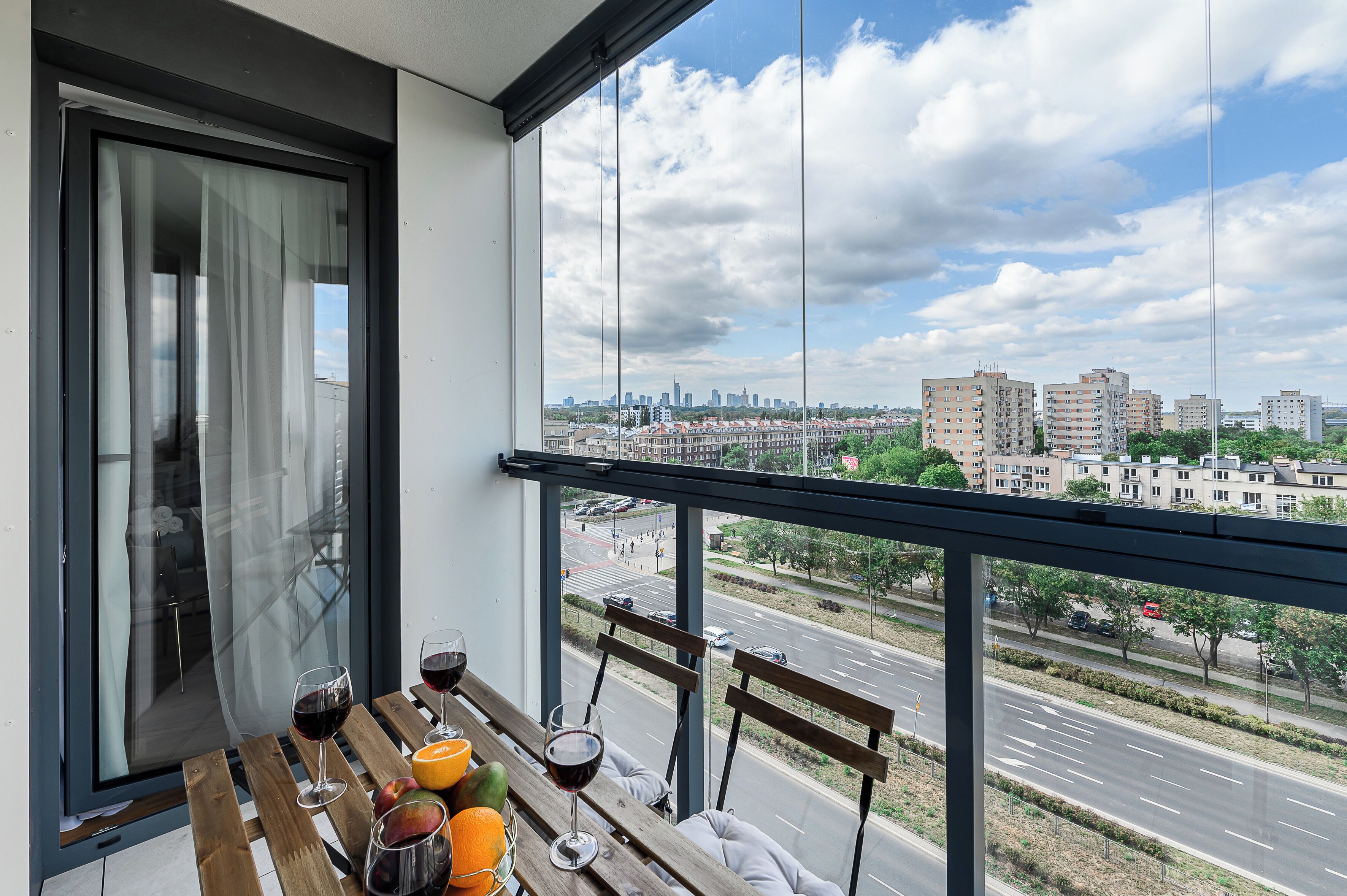 A balcony with a city view, a table with drinks, and a chair.