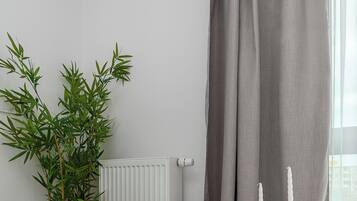 Een moderne kamer met een witte stoel, een klein rond tafeltje met een boek, een bamboeplant en een radiator.
