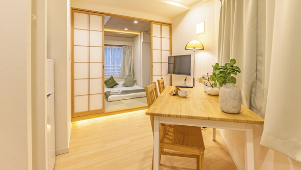 Ein Hotelzimmer mit Holzboden, einem Esstisch mit Stühlen, einem Fernseher, einer Lampe und einer Topfpflanze.