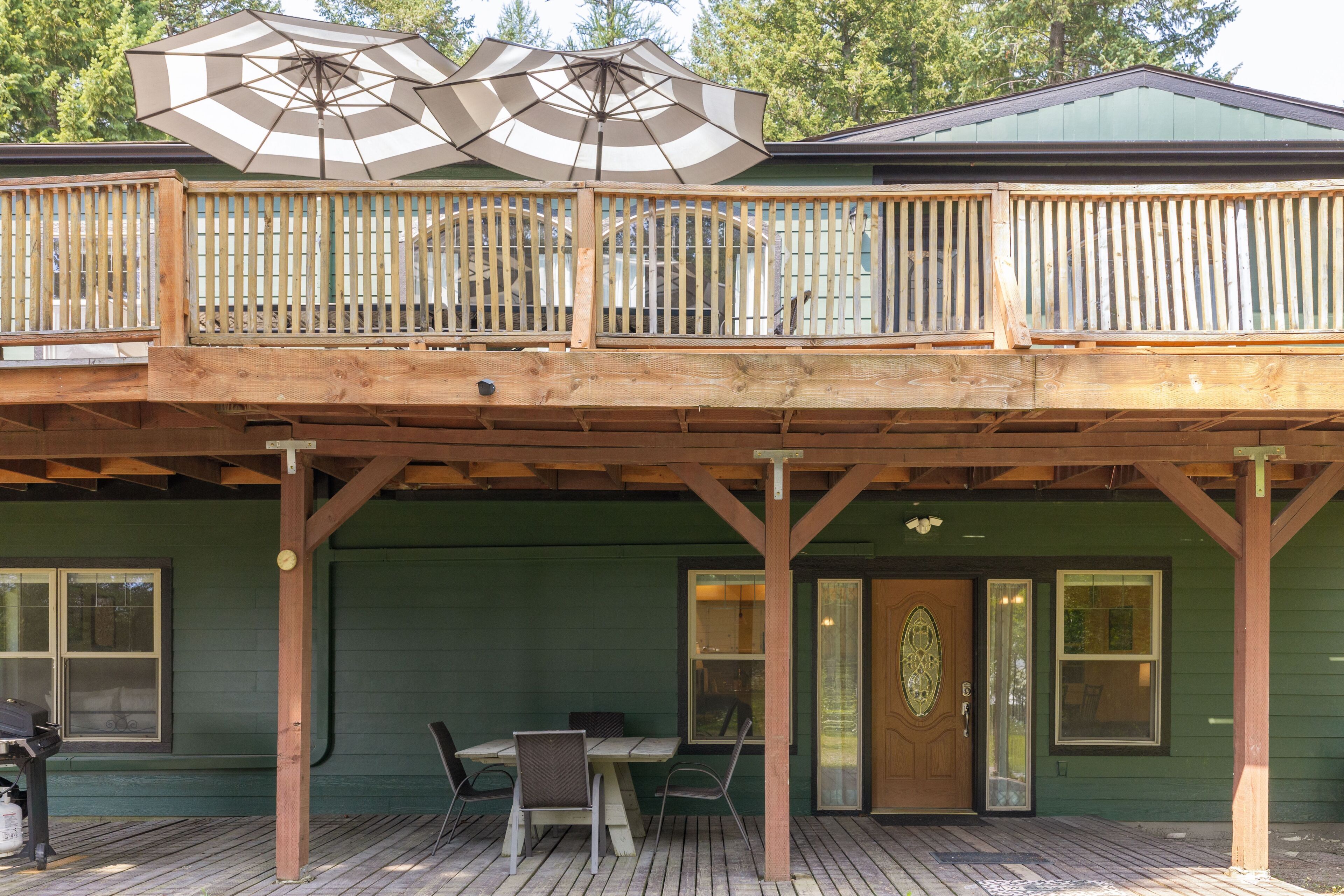 A wooden deck with a table and chairs, a covered area with umbrellas, and a green building with windows.