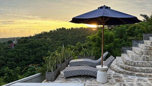 A poolside area with a stone staircase, black and white patterned cushions, and an umbrella.