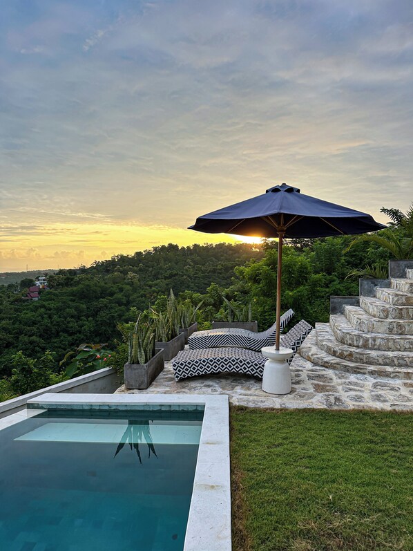 Zona junto a la piscina con una escalera de piedra, cojines con estampado blanco y negro, y una sombrilla.
