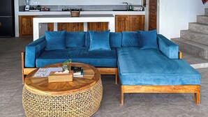 A modern living area with a blue sectional sofa, a woven coffee table, and hanging wicker lamps.