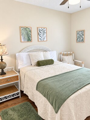 Une chambre à coucher avec un lit, une table de chevet, une lampe et une œuvre d’art accrochée au mur.