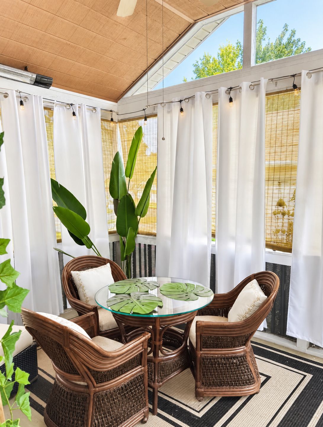 A covered patio area with wicker furniture, a glass table, and white curtains.
