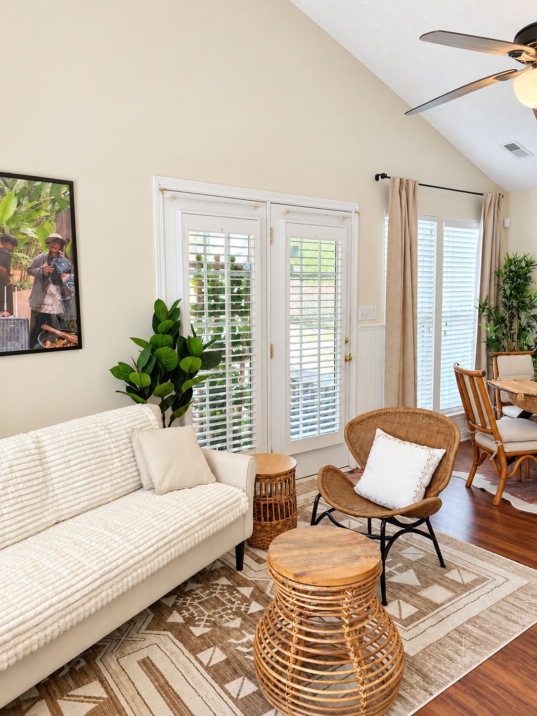 A living room with a sofa, wicker chairs, a round wooden table, and a large plant.