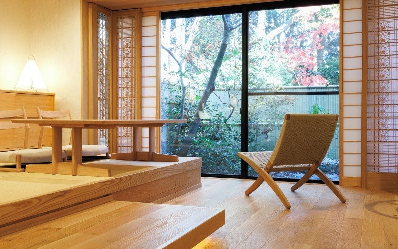 A traditional Japanese room with tatami flooring, a low table, a cushioned chair, and a sliding door leading to a garden.