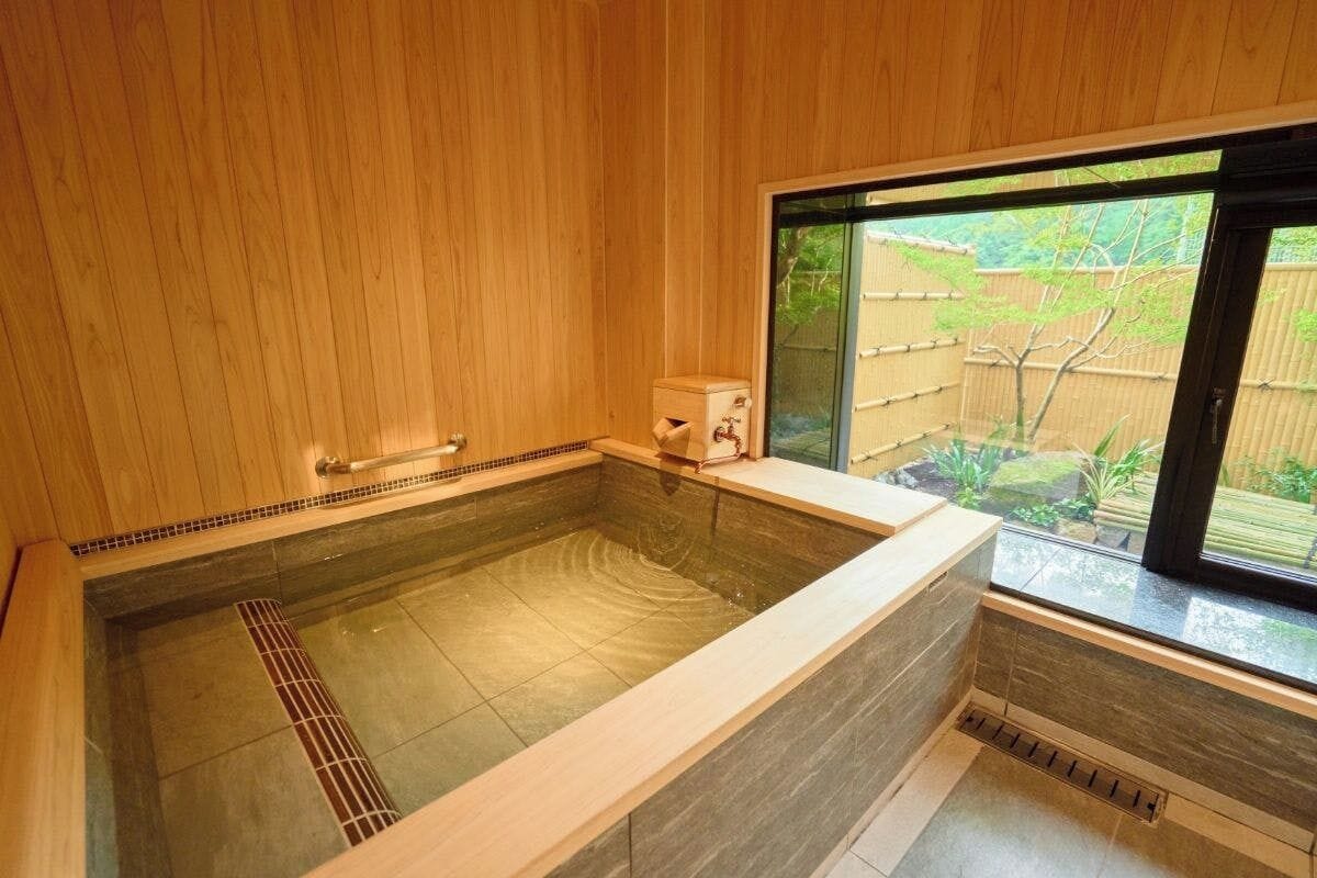 Ein Holzinnenraum mit einer großen Badewanne, einem Fenster und einem kleinen Heizgerät.