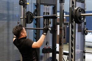 A person using a weightlifting machine in a gym with a large window in the background. - Ryoso SUIUNTEI (Asakura)