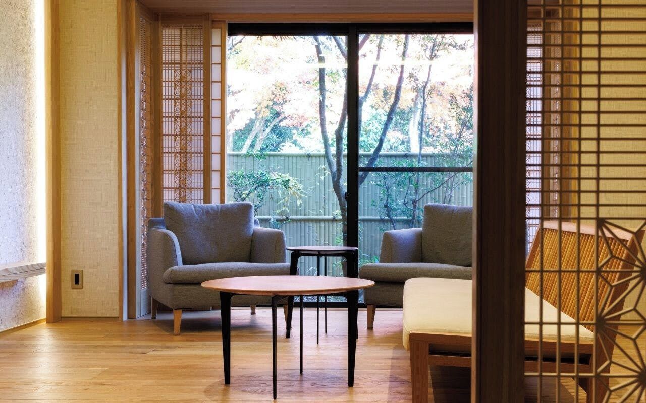 A room with two sofas, a small table, and a sliding door leading to an outdoor area with a view of trees and a fence.