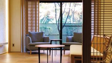 A room with two sofas, a small table, and a sliding door leading to an outdoor area with a view of trees and a fence.
