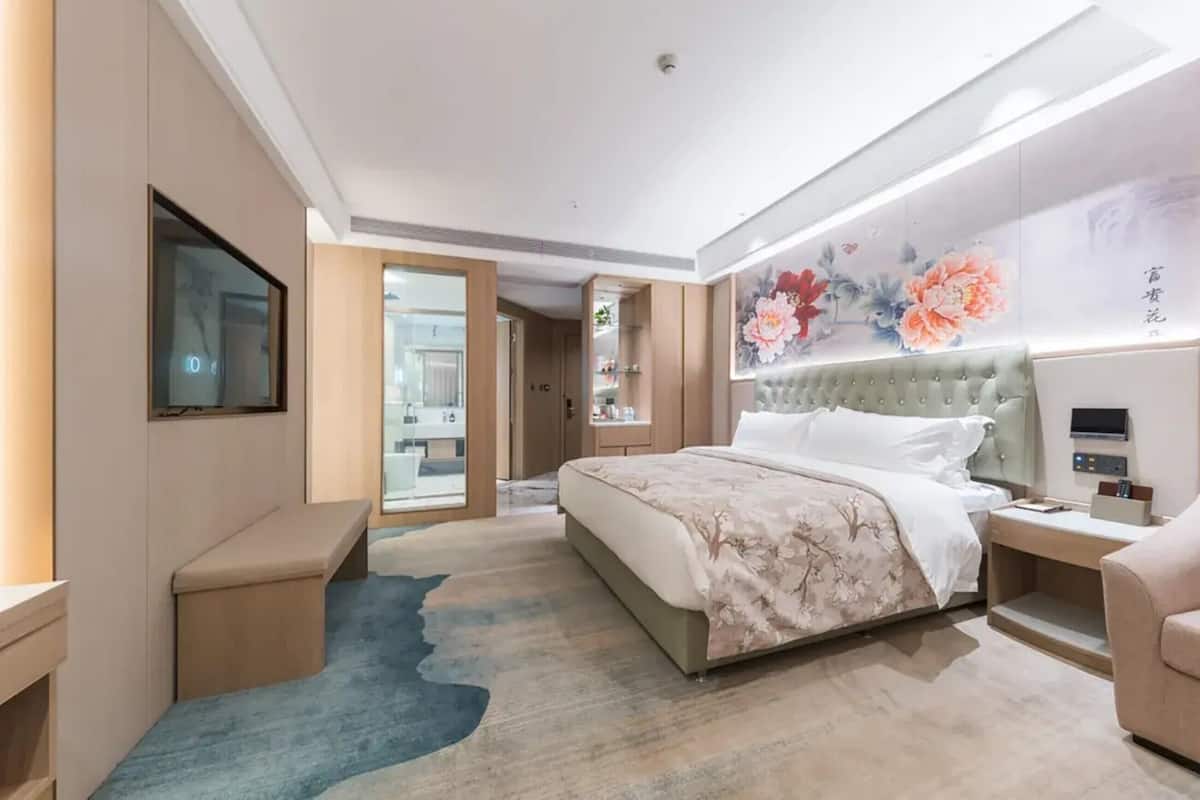 Habitación de hotel moderna con una cama grande, un televisor de pantalla plana, una mesita de noche y un panel de control instalado en la pared.