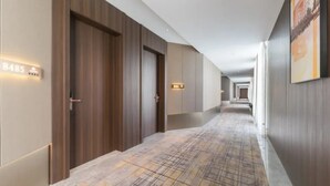 A modern hotel hallway with wooden paneling, a patterned floor, and a long corridor leading to a door marked '8485'. - Shengbaolong International Hotel (Wuhan)