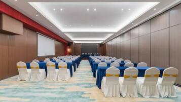 A conference room with rows of tables and chairs, a projector screen, and a carpeted floor.