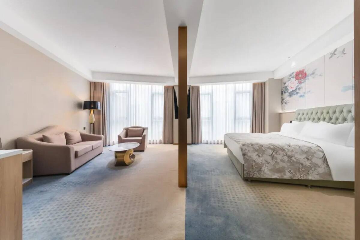 Una habitación de hotel con cama, sofá, sillón, una mesita y televisor.