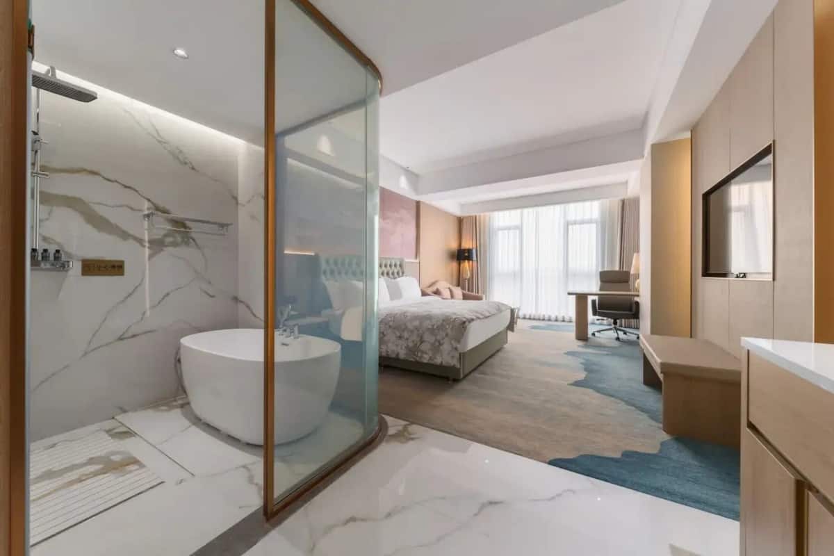 Una habitación de hotel moderna con baño de mármol, una cama con cabecera, un escritorio y un televisor.