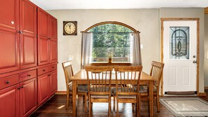 Ein Essbereich mit einem Holztisch und -stühlen, einem großen roten Schrank, einer Uhr und einer Tür mit einem Glasfenster.