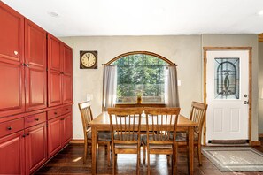 A dining area with a wooden table and chairs, a large red cabinet, a clock, and a door with a stained glass window. - Hungry Horse Hideout - Upper Level with Hot tub (Hungry Horse)
