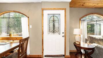 A room with a wooden door, a dining table with chairs, a sofa, and a lamp.