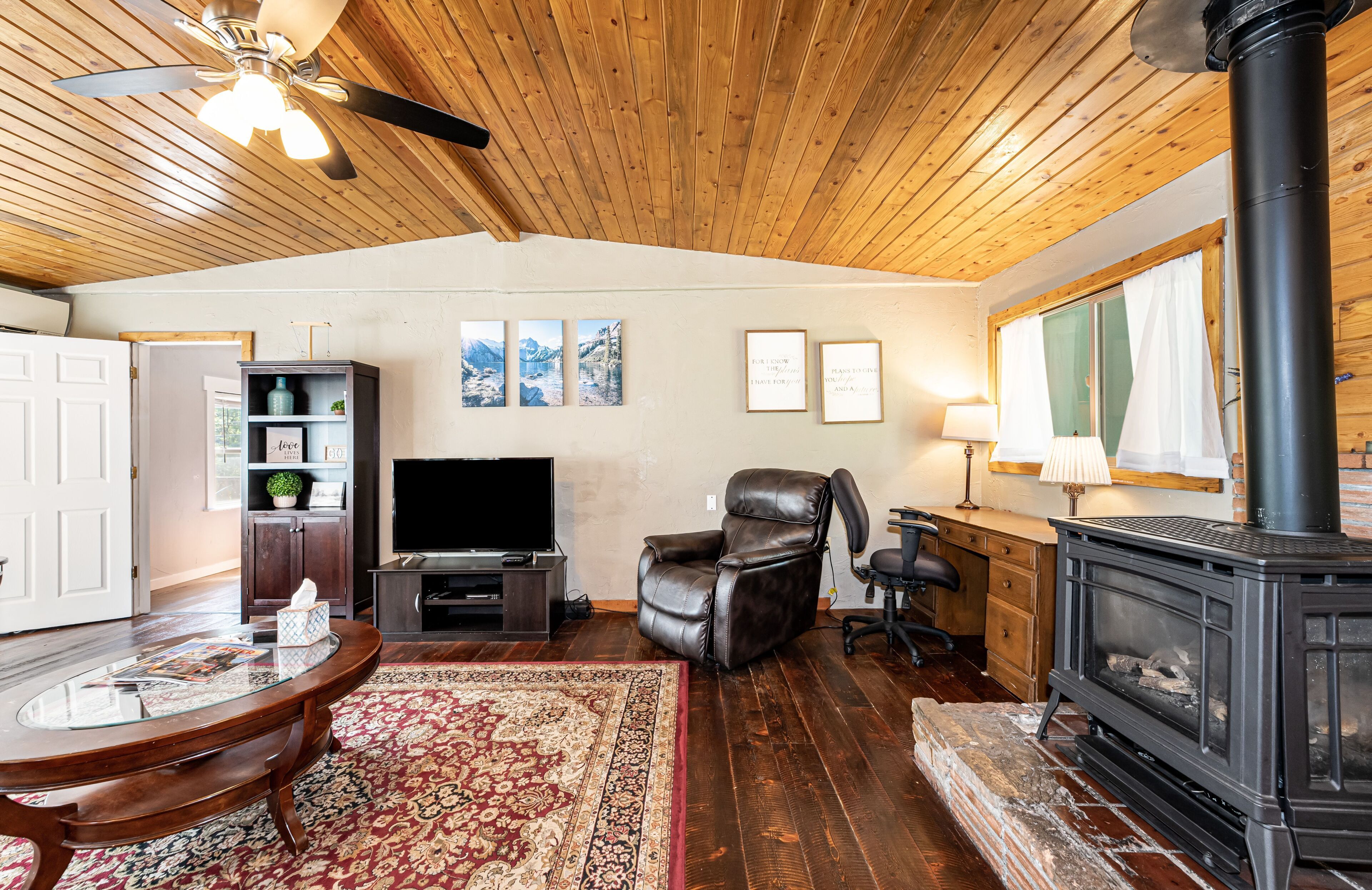 A cozy living room with a fireplace, a leather recliner, a flat-screen TV, and a wooden ceiling.