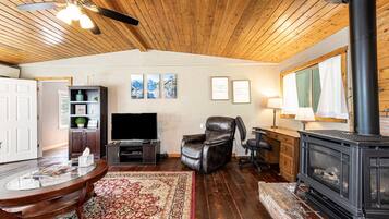 A cozy living room with a fireplace, a leather recliner, a flat-screen TV, and a wooden ceiling.