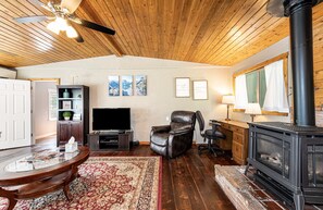 A cozy living room with a fireplace, a leather recliner, a flat-screen TV, and a wooden ceiling.