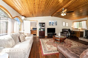 A spacious living room with a wooden ceiling, a large flat-screen TV, a leather armchair, a sofa, and a coffee table. - Hungry Horse Hideout - Upper Level with Hot tub (Hungry Horse)