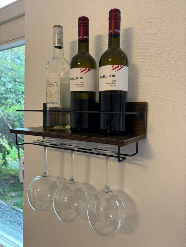Three wine bottles on a shelf with three wine glasses below.