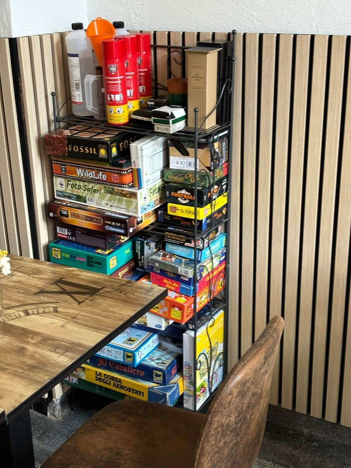 A storage rack filled with various board games and a small table with a wooden surface.
