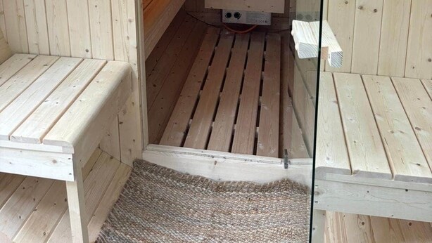 A sauna with wooden walls, benches, a bench heater, and a glass door.