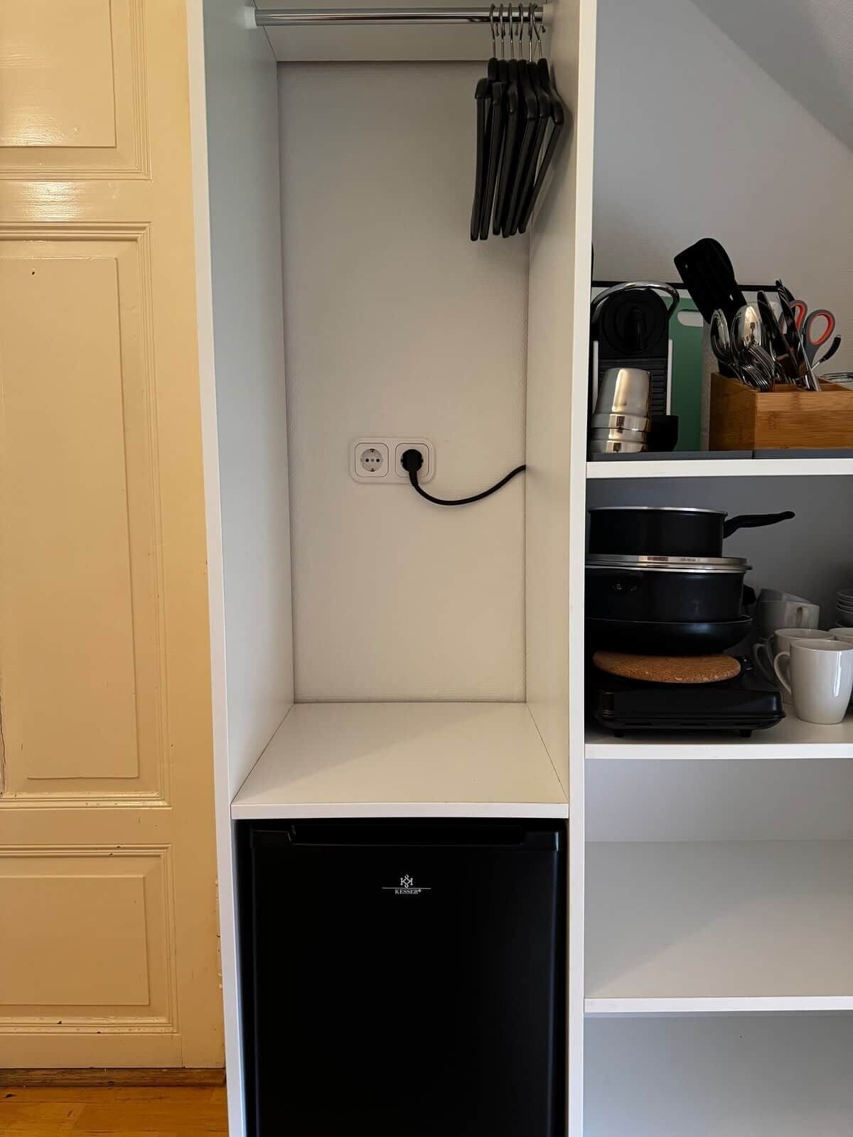Cocina compacta con lavavajillas integrado, un perchero con utensilios y una cafetera en la encimera.